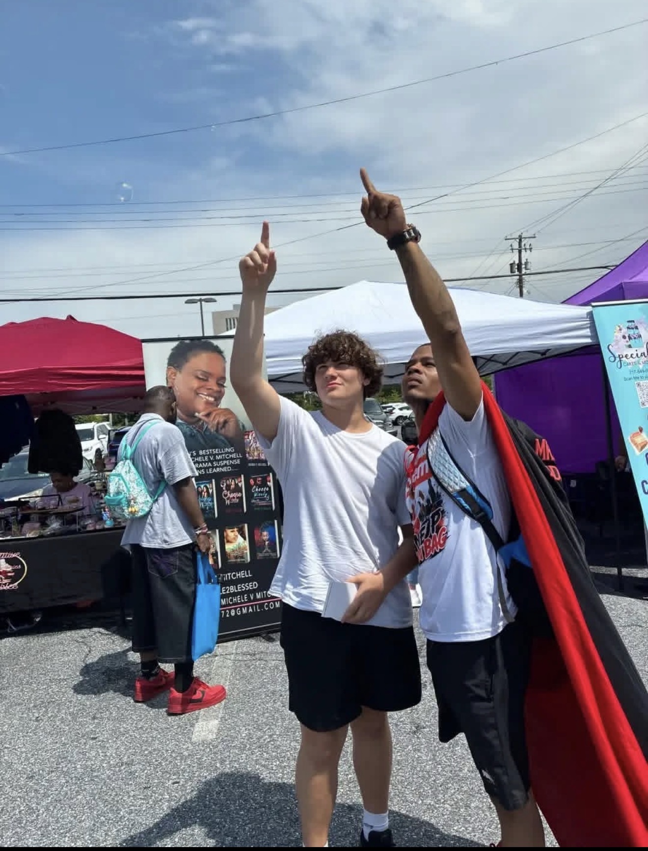 Mr. Supreem in a red cape pointing to the sky with a young man at a community market